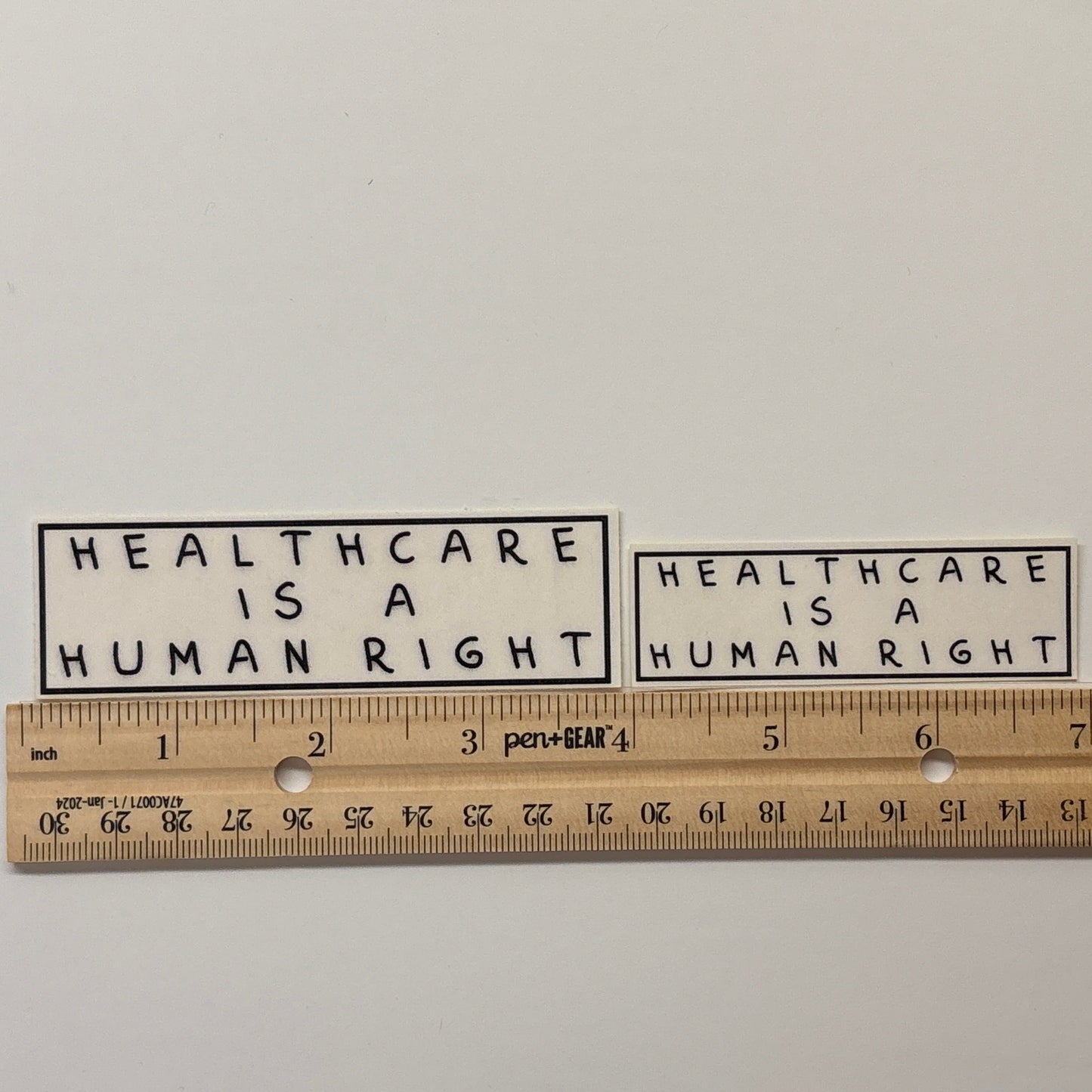 Two stickers with 'Healthcare is a human right' text on a white background, with a ruler for scale.