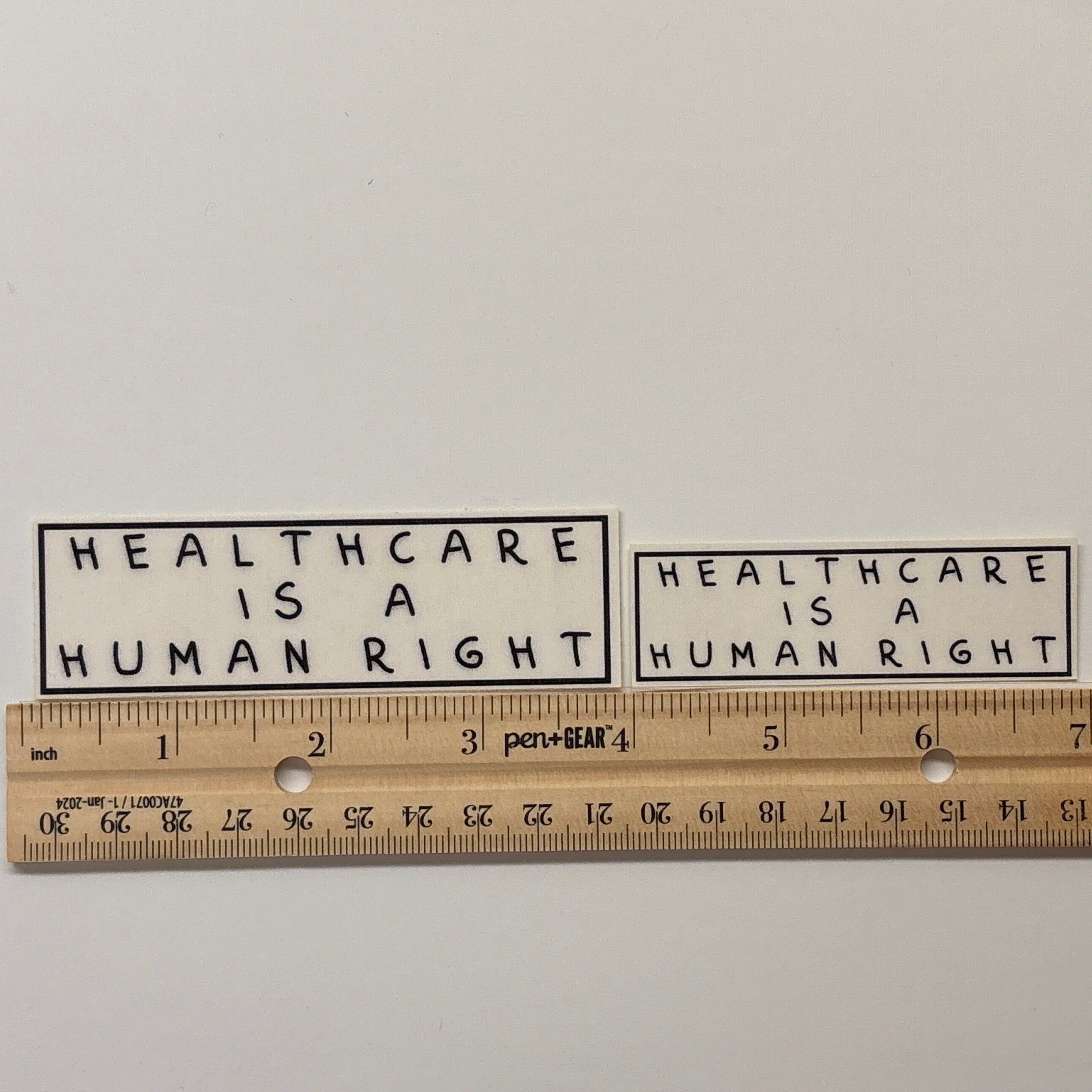 Two stickers with 'Healthcare is a human right' text on a white background, with a ruler for scale.