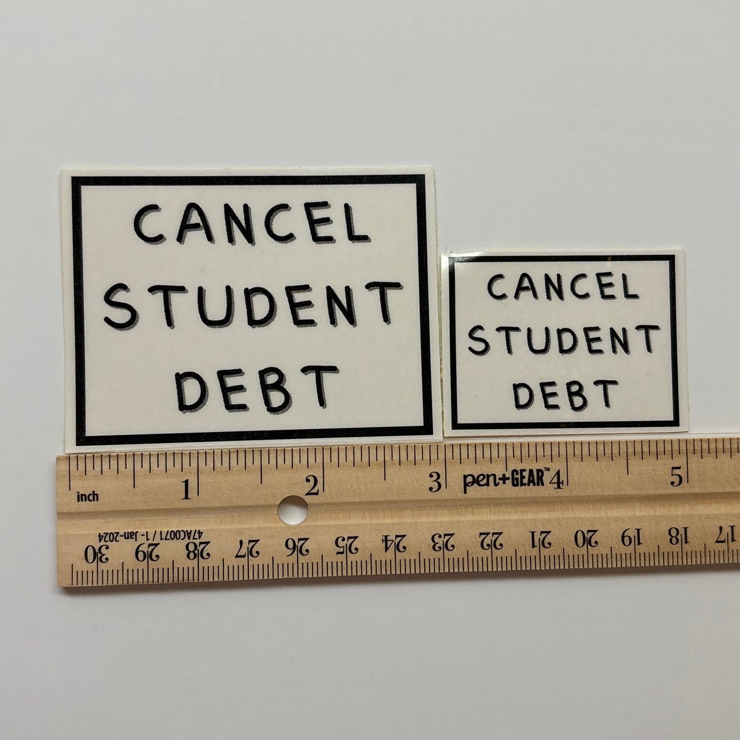 Two 'Cancel Student Debt' posters on a white surface with a ruler for scale.