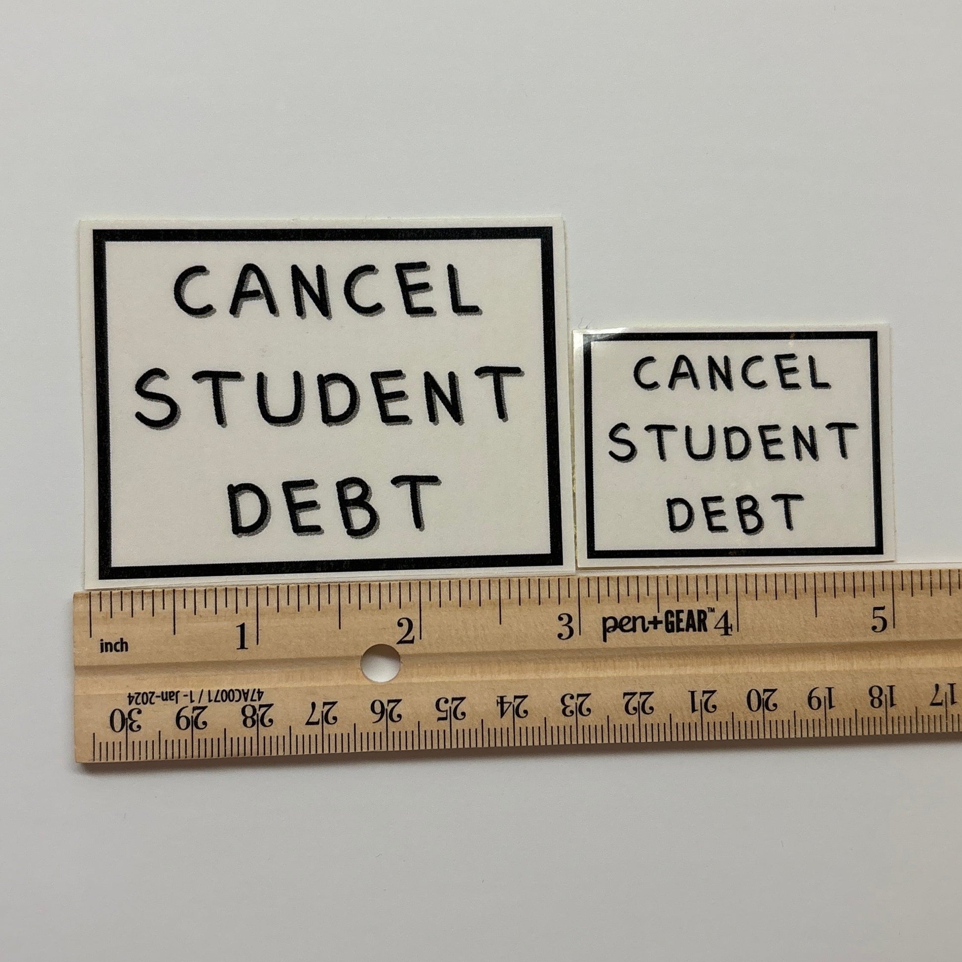 Two 'Cancel Student Debt' posters on a white surface with a ruler for scale.