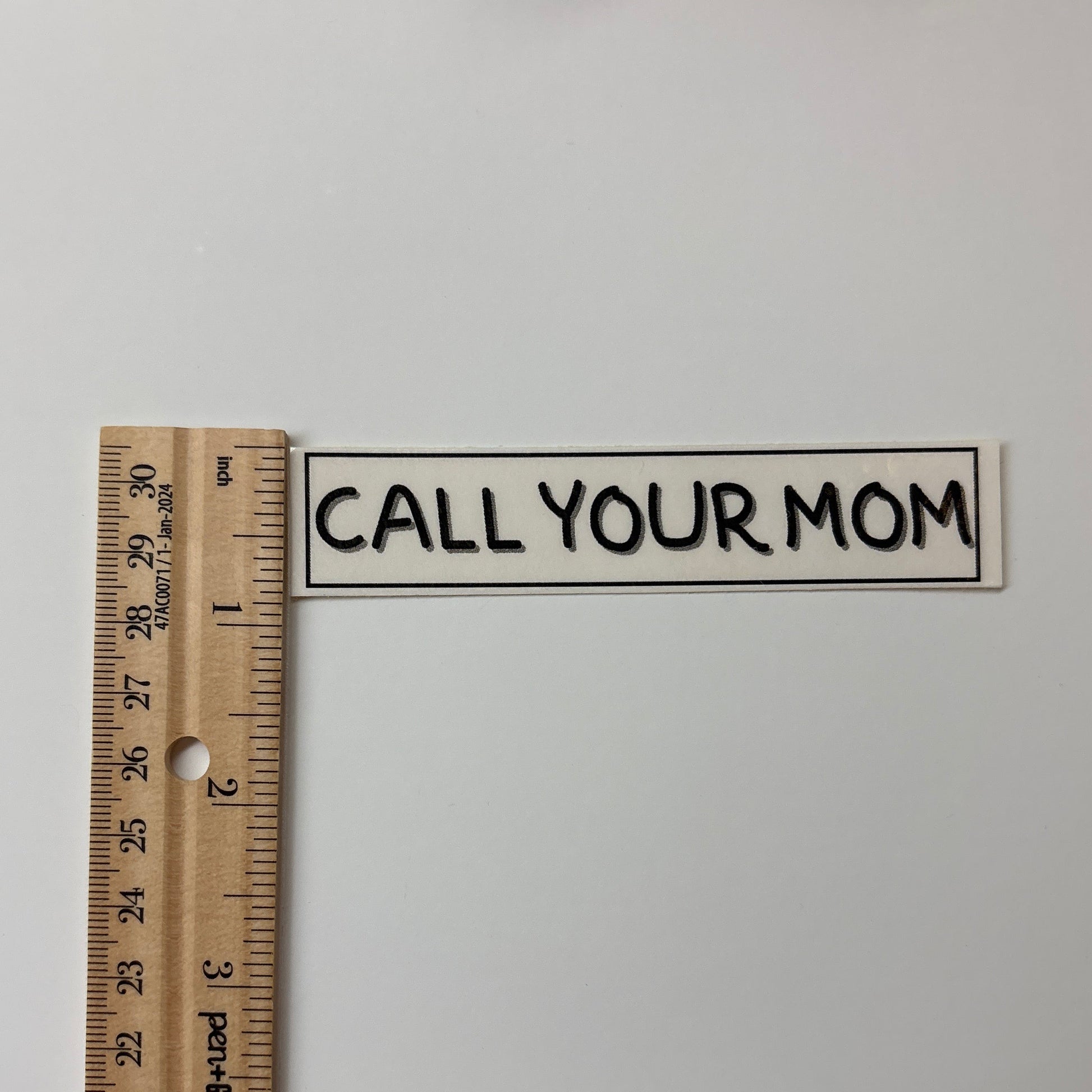 Small sign with 'CALL YOUR MOM' text on a white background, accompanied by a ruler for scale.