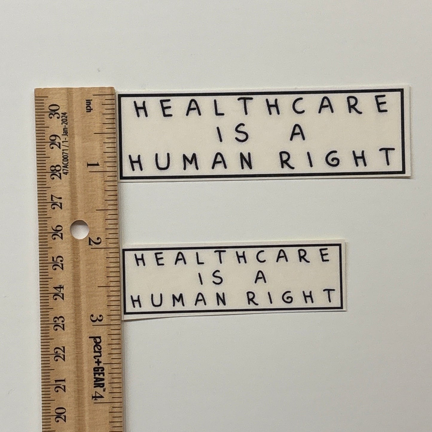 Two stickers with 'Healthcare is a Human Right' text on a white background, with a ruler for scale.