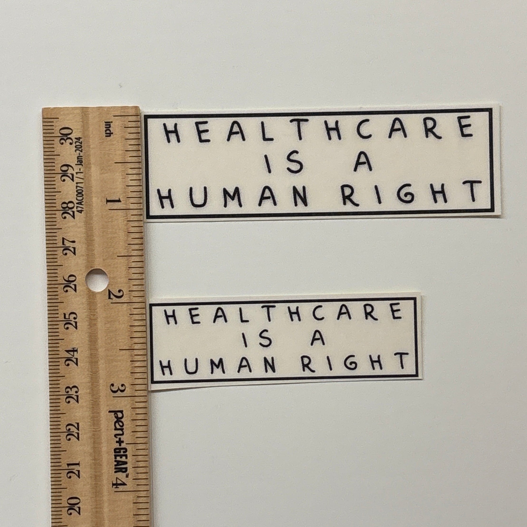 Two stickers with 'Healthcare is a Human Right' text on a white background, with a ruler for scale.